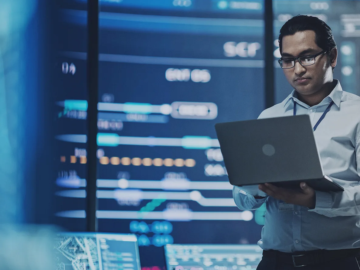 Man holding a laptop in a data center for managed XDR services.